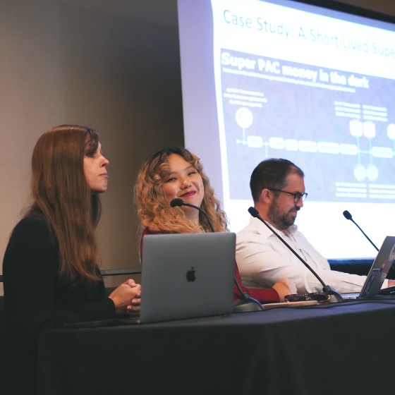 Three people sit in front of a presentation screen in a conference room. They are giving a presentation about open source intelligence.